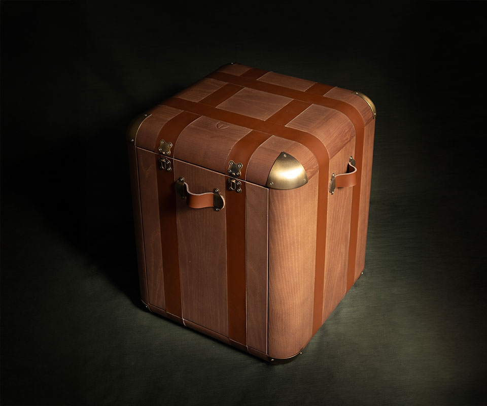 45º front view of the Burke chair featuring a walnut wood structure, saddle leather details, and aged brushed brass accents, set against a green background with dramatic lighting.