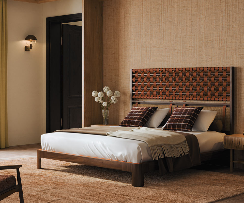 Faraday wall lamp in smoked walnut wood and brass details set in a bedroom with Élitis Abaca wallpaper and a rug by Kelly Wearstler. The space also includes an O'Connell II Bed with a headboard featuring leather details in Prestige fabric from Élitis, Ralph Lauren Wallace throw pillows.