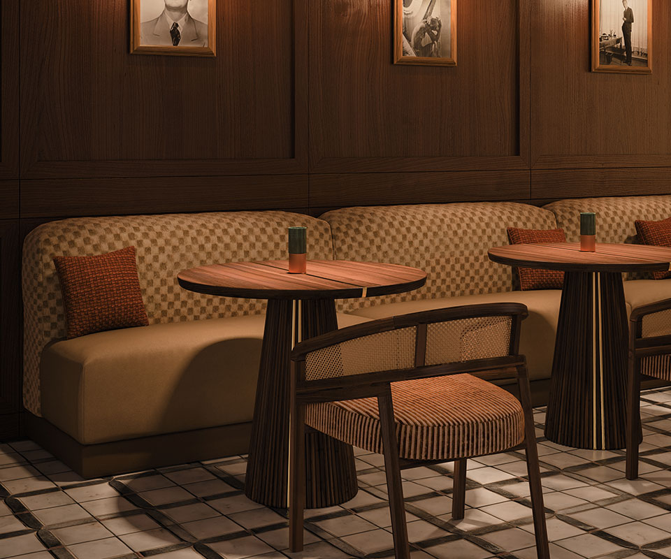 Spencer dining chair upholstered in striped fabric, with a smoked walnut wood structure and rattan details, in a restaurant setting with mood lighting, next to the Henry dining table.