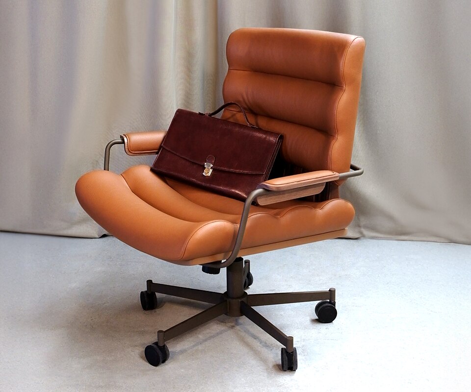 Thomas I office chair in orange genuine leather, paired with smoked walnut wood, powder-coated stainless steel, and lacquered wood, shown in a setting with a work briefcase.