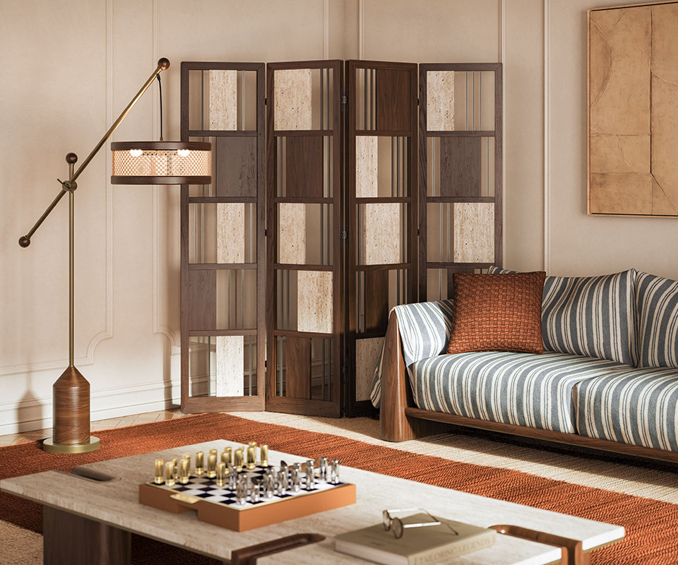 Living room interior featuring the Wordsworth folding screen in smoked walnut wood, travertine, and brass; Hamilton floor lamp in smoked walnut and brass; Dudley sofa in striped fabric; and Grenville center table. The space showcases warm tones throughout.
